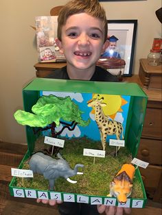 a young boy holding up an open box with fake animals in it and pictures on the inside