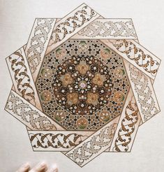 a hand is holding up a drawing with intricate designs on the paper in front of it