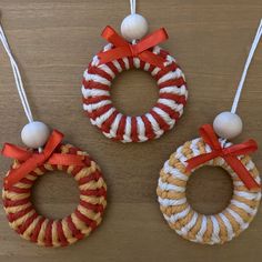 three handmade christmas wreaths hanging from strings on a wooden table with red and white ribbons