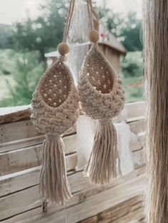 two crocheted earrings hanging from a rope on a wooden porch swing with trees in the background