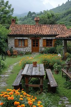 a wooden table sitting in the middle of a garden next to a stone building with windows