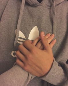 a person wearing a adidas hoodie with their hands on the wrist and holding an object