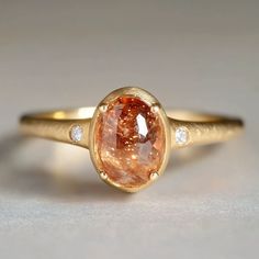 **Capture the warmth of the sun with our beautiful engagement ring, featuring a radiant sunstone at its center and two accent diamonds on either side. *Gem - 6*9.5mm Sunstone, 2mm diamond Finish: Brush finish *Gems: The natural gems natural hues vary, adding an organic touch to your ensemble. I'll try to select them in the spectrum as close to the picture as possible. Want to see your specific stone? Just send me an email, and I'll happily provide photos for you to choose from. *Metal: Delicatel Raw Rings Engagement, Colorful Vintage Engagement Rings, Matte Gold Ring, Engagement Ring Without Diamond, Funky Wedding Ring, Non Engagement Rings, Ring Shape For Hand Type, Gold Gemstone Wedding Rings, Engagement Rings With Stones