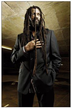 a man with dreadlocks standing in front of a wall wearing a suit and tie