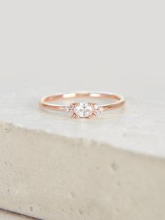 a rose gold ring with three diamonds on the side, sitting on top of a stone block