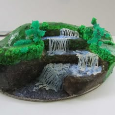 a cake shaped like a waterfall with trees and grass on it's sides, sitting on a table