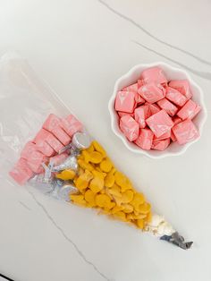 two bags of marshmallows next to a bowl of yellow and pink candies