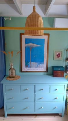 a painting hangs above a blue dresser in a room