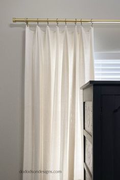 a white curtain hanging on the side of a wall next to a black cabinet with drawers