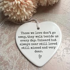 a heart shaped ceramic ornament with a quote on it and flowers in the background