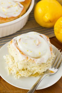 a piece of lemon roll on a plate with a fork next to it and two lemons in the background