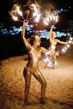 two women in gold bodysuits are holding sparklers on the beach at night