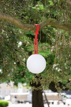 a white ball hanging from a tree with a red ribbon on it's end