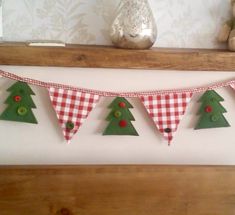 a christmas tree banner hanging on a mantle with other decorations in the background and a teddy bear next to it