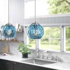 two blue glass globes hanging from a kitchen ceiling over a sink and countertop