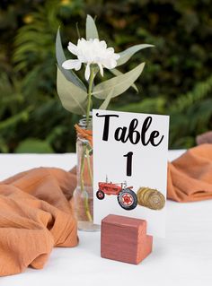 a table number sign with a flower in a glass vase on top of a wooden block