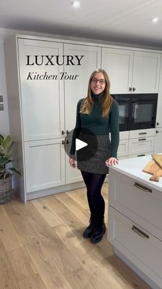 a woman standing in a kitchen with white cabinets and wood flooring, smiling at the camera