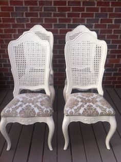 two white chairs sitting next to each other on top of a wooden floor in front of a brick wall