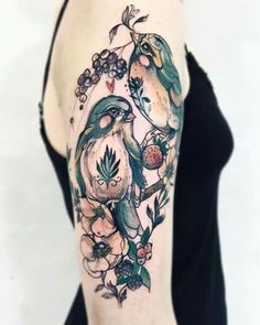 a woman's arm with two birds on it and flowers around the arm, in front of her