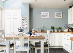 a kitchen with blue walls and white cabinets is pictured in this image, there are two chairs at the table