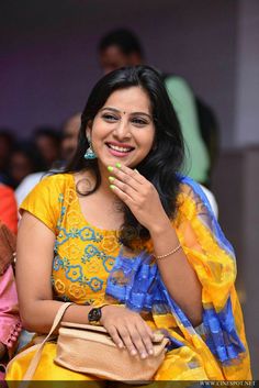 a woman sitting down with her hand on her face and smiling at the camera while holding a purse