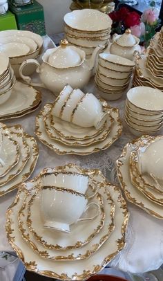 a table topped with lots of white and gold china plates, cups and saucers