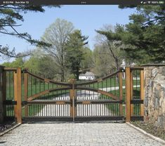 an iron and wood driveway gate with brick pavers walkway leading up to the entrance