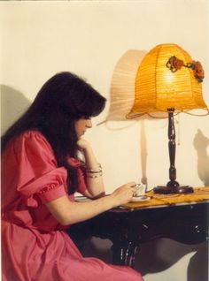 a woman sitting in front of a desk with a lamp on it's side