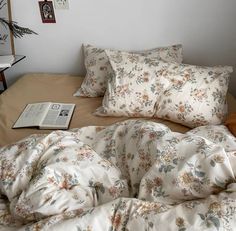 an unmade bed with flowers on it and a book sitting on the side table