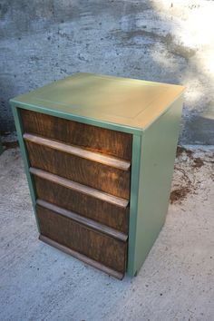 a green and brown cabinet sitting on top of a cement floor next to a wall