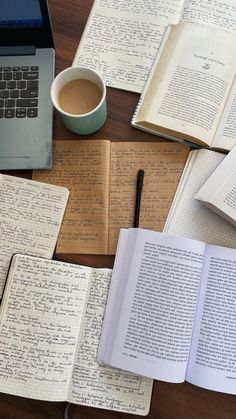 an open book sitting on top of a wooden table next to a laptop computer and cup of coffee