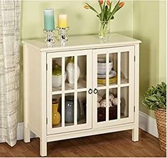 a white cabinet with glass doors and flowers on the top, next to a potted plant