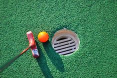 an orange golf ball sitting next to a hole in the grass with a driver's club