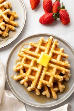 two plates with waffles and strawberries on the side, one has a piece of butter