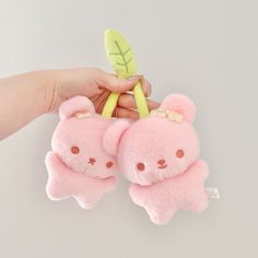 two small pink teddy bears are held up by a person's hand with a green leaf