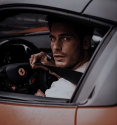 a man sitting in the driver's seat of a sports car with his hand on the steering wheel