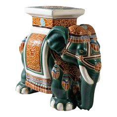 an elephant statue sitting next to a vase on a white background with orange, blue and green designs