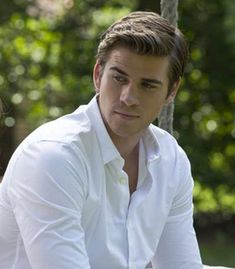 a man in white shirt sitting next to a tree with his hands on his hips