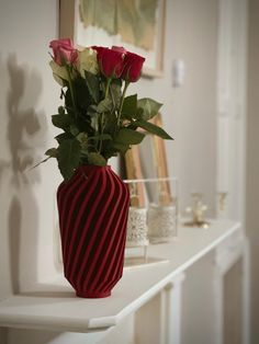 a red vase with roses in it sitting on a white shelf next to a mirror