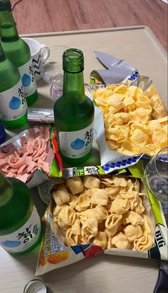 the table is full of snacks and drinks on it, along with two empty beer bottles