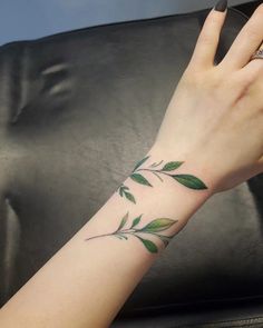 a woman's hand with a green leaf tattoo on her left arm and wrist