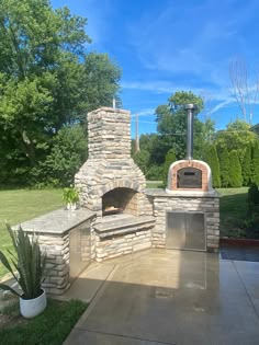 an outdoor stone pizza oven in the middle of a yard with a potted plant