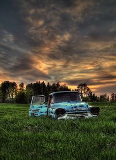 an old pickup truck sitting in the middle of a grassy field under a cloudy sky