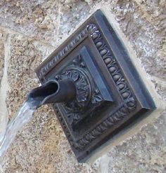 a water fountain spouting from the side of a stone wall