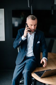 a man sitting at a table talking on a cell phone and holding a laptop computer