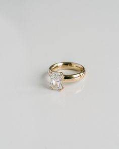 a yellow gold engagement ring with a princess cut diamond in the center, on a white background