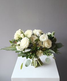 a bouquet of white flowers sitting on top of a white cubed vase filled with greenery