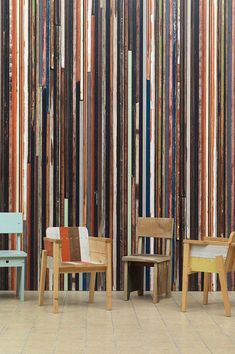 three wooden chairs sitting next to each other in front of a wall with multicolored stripes