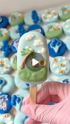 a hand holding a green and blue popsicle in front of some cupcakes