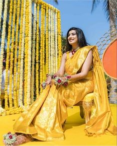 a woman in a yellow sari sitting on a bench with flowers and garlands